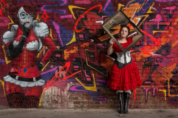 Frau in rotem Kleid neben Graffiti schaut durch einen Bilderrahmen